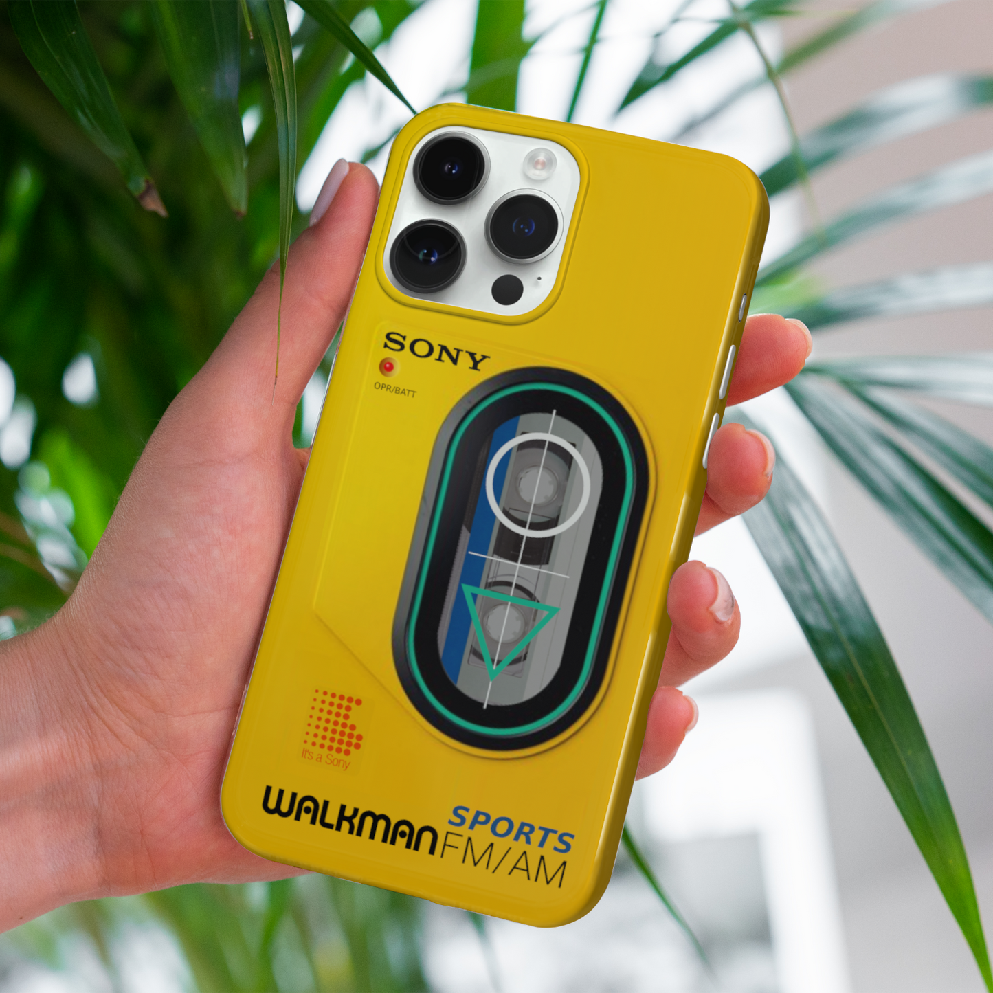 Yellow phone case with Sony Walkman design held by a hand against a blurred green leafy background